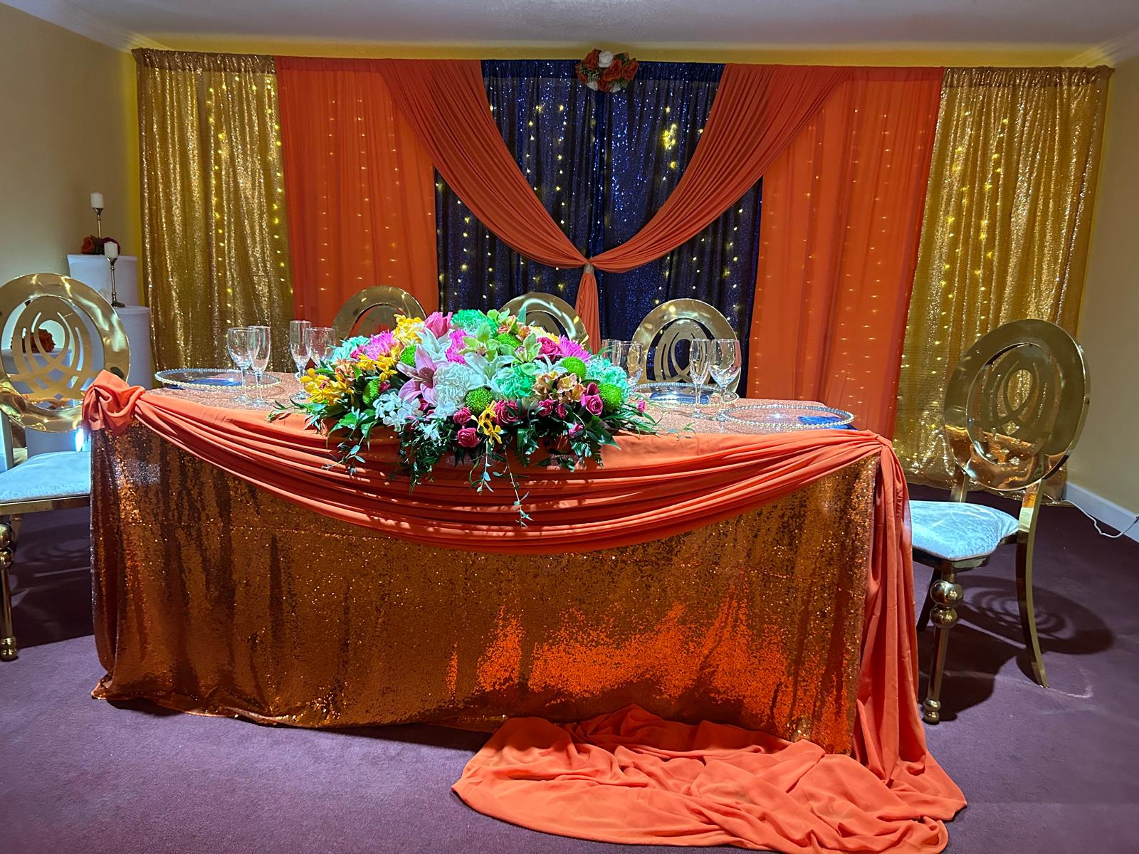 Banquet hall head table decorated for a wedding reception with gold chairs and floral centerpieces.