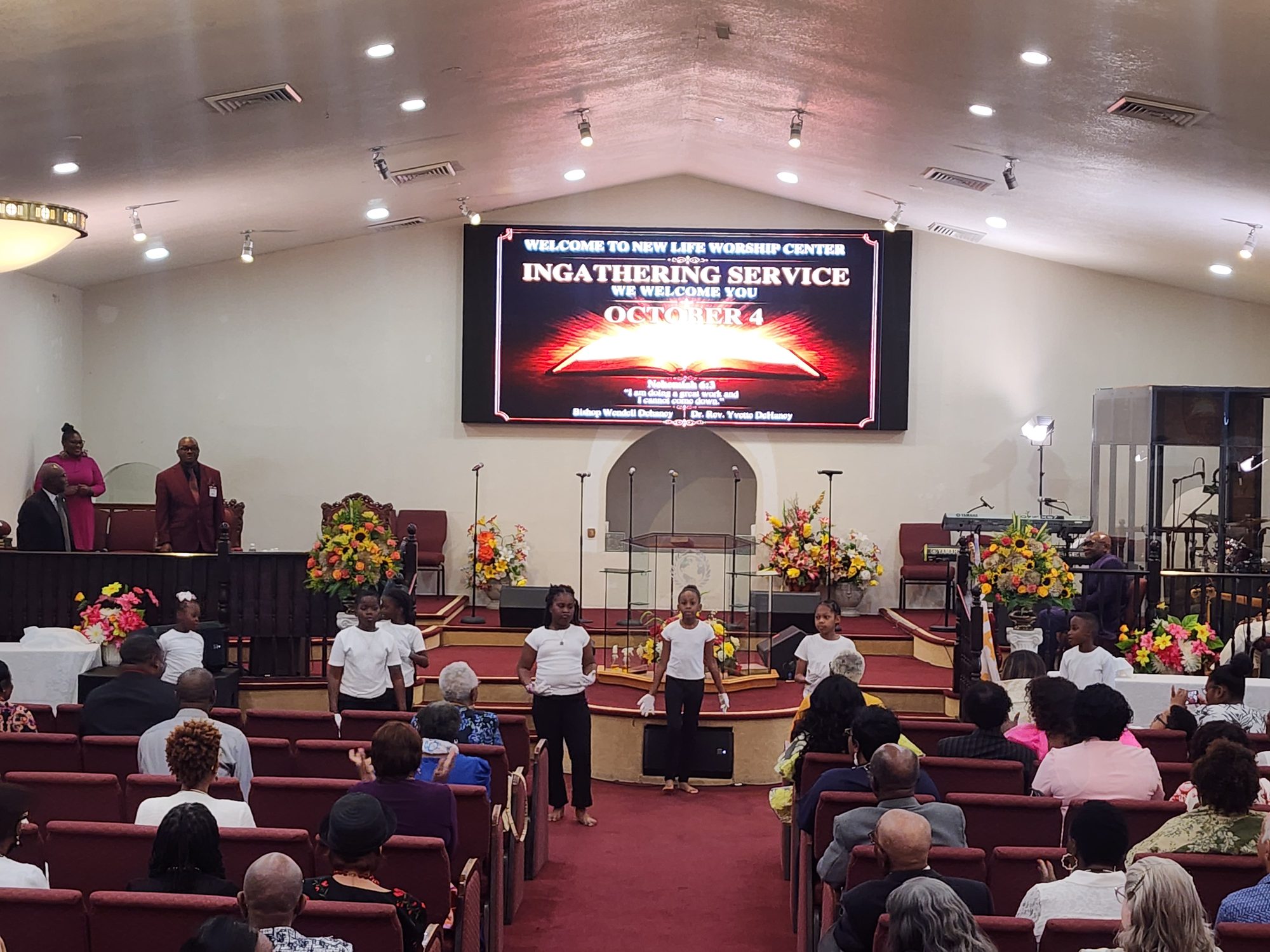 Sanctuary view during the Ingathering service with welcome screen and children on stage.